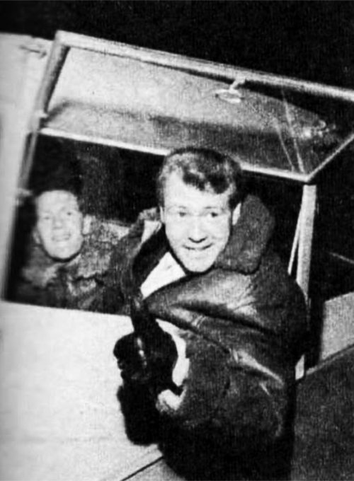 A man in a flying jacket leans out of a cockpit