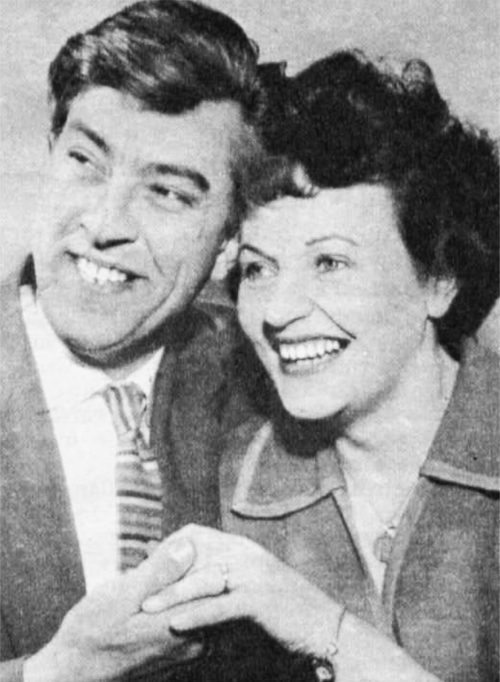 Two people hold hands romantically while beaming off to the side of the camera