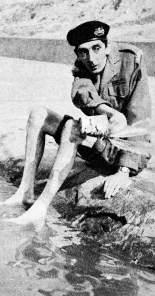 A man in uniform with his trousers rolled up and his feet in the sea