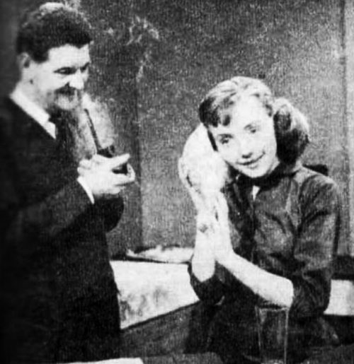 A man smoking a pipe watches a woman listening to a shell