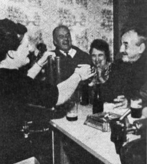 A woman hands a glass to a man over a bar